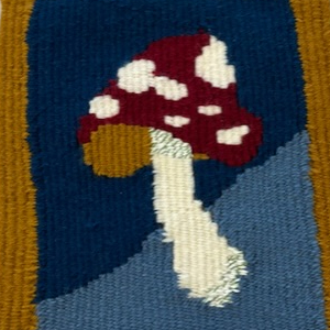 A tapestry weaving of a red and white spotted mushroom