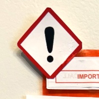 A collage of medication information packets and orange transparent film. A letter made up of snippets of text from different sources informs the reader that they have failed to meet the requirements of society, listing the reasons below, and that treatment will be performed. Other vaguely ominous instructions regarding the treatment that is to be performed follow. The letter is mounted on an orange rectangle cut from orange transparent film, evoking a bottle of medication. In the background is a sheet of paper listing a multitude of concerning side effects.