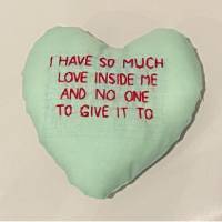 A stuffed pastel green fabric heart in the style of a Conversation Heart candy. The red text, in all caps, reads: I have so much love inside me and no one to give it to